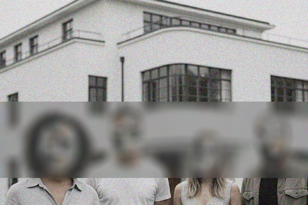 A white, modernist-style building with large windows and a curved corner. The lower portion of the image is blurred, obscuring several people standing in front of the building.